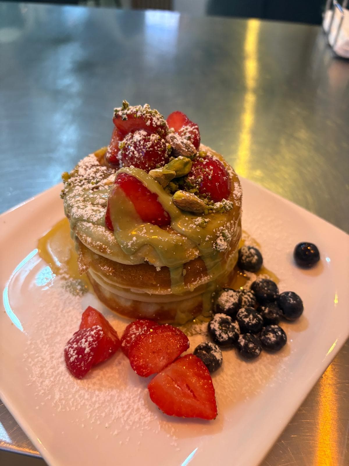 Pancakes mit Pistaziencreme, Pistazien, Erdbeeren und Heidelbeeren auf einem Teller